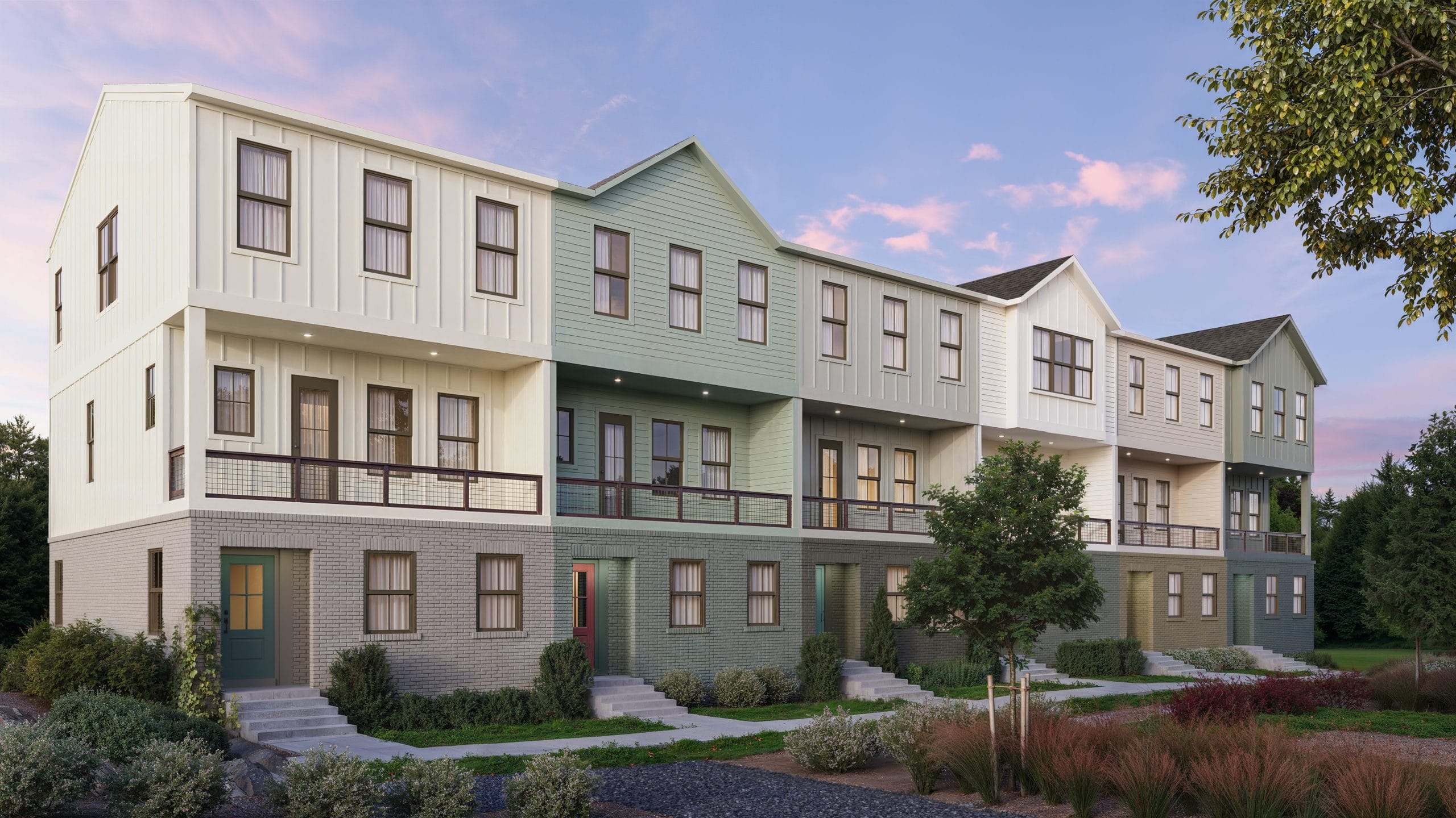 Multi-story townhouses with light green and beige exteriors, large windows, balconies, small front yards, clear sky with clouds, trees and shrubs.