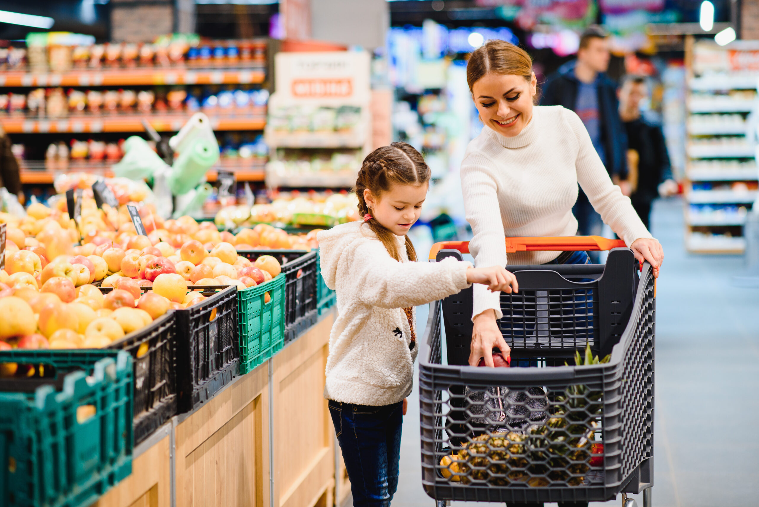 Family in the supermarket. Beautiful young mom and her little daughter smiling and buying food. The concept of healthy eating. Harvest
